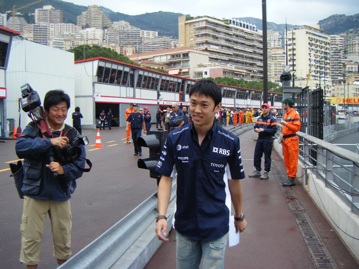 Kazuki Nakajima im dunkelblauen Williams-Teamhemd geht beim GP Monaco 2008 an der Boxengasse entlang, links ein Fotograf mit Kamera