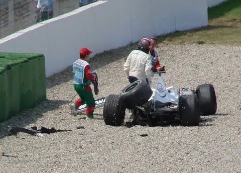 Jacques Villeneuve geht beim GP Deutschland 2006 neben seinem verunfallten BMW Sauber im Kiesbett, daneben ein Streckenposten.